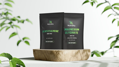 Two black supplement pouches from Nutrality, Benfotiamine 500 MG and Magnesium Glycinate 500 MG, displayed on a wooden stand with a soft-focus background of green leaves.